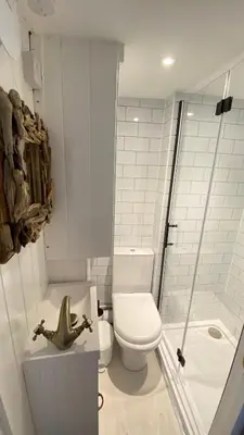 a white bathroom with a toilet and a shower at SMUGGLERS HIDE or SMUGGLERS CABIN - EITHER a 2 Bedroom FISHERMANS COTTAGE with Childs Bunk and HARBOUR VIEWS - OR a ground floor private small CABIN ROOM - 10 Metres To Sea Front - Book Both for a 3 Bed House - 2023 GLOBAL REFURBISHMENT AWARD WINNER in St Ives