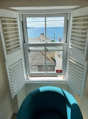 a window with a blue chair looking out at the ocean at Luxury Modern Suite in Marazion with Parking in Marazion