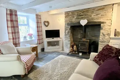 a living room with a stone fireplace and a tv at Stable Cottage in Delabole