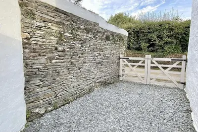 a stone wall with a white gate and a fence at Stable Cottage in Delabole