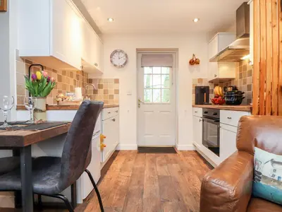 a kitchen with white cabinets and a table with chairs at Inny Brook Cottage in Camelford