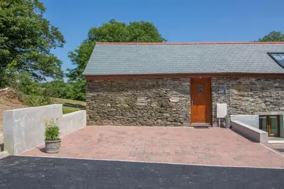 a stone building with a wooden door and a patio at Hendra Retreat Owls Roost Cottage North Cornwall in Camelford