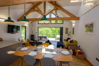 a dining room and living room with a table and chairs at Tresillian Lodge Waterfront, Forest, Hot tub,Sauna in Truro