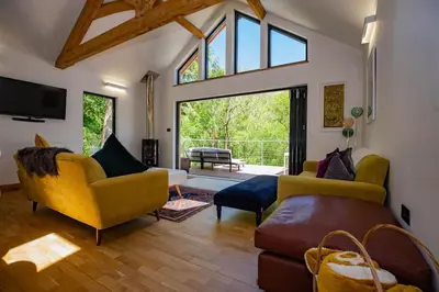 a living room with yellow furniture and a large window at Tresillian Lodge Waterfront, Forest, Hot tub,Sauna in Truro
