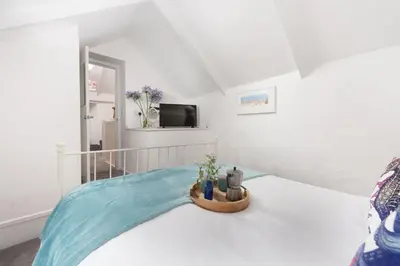 a white room with a bed with a blue blanket at Shell Cottage, St Ives in St Ives