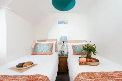 two beds in a bedroom with a bowl of fruit on a table at Shell Cottage, St Ives in St Ives