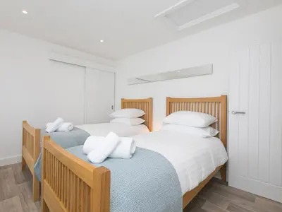 two beds in a bedroom with white walls and wood floors at Samphire in St Ives