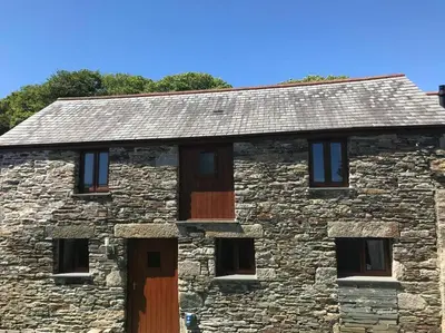 an old stone building with wooden doors and windows at Hendra Retreat Piglets Cottage North Cornwall in Camelford