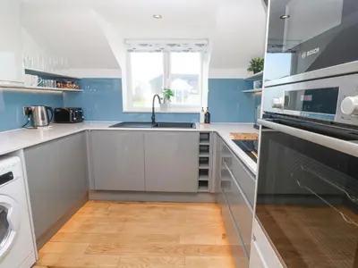 a kitchen with white cabinets and a sink and a window at Island View in Newquay