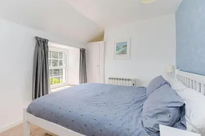 a bedroom with a bed with a blue comforter and a window at Stokes Cottage in Wadebridge