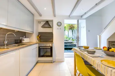 a kitchen with white cabinets and a counter with yellow chairs at Stokes Cottage in Wadebridge