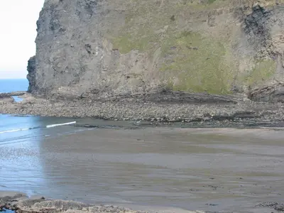 a beach with a rocky cliff and the ocean at Woodgate in Bude