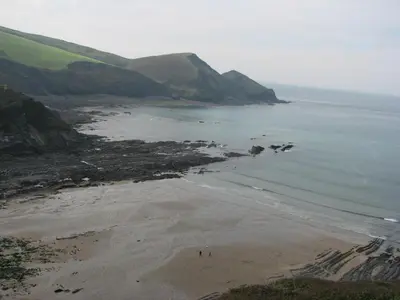 a beach with people walking on the sand and the water at Woodgate in Bude