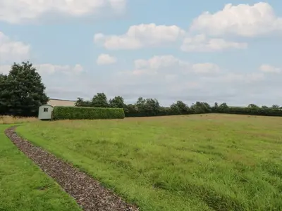a field of grass with a white building in the distance at Flora's Hut in Liskeard