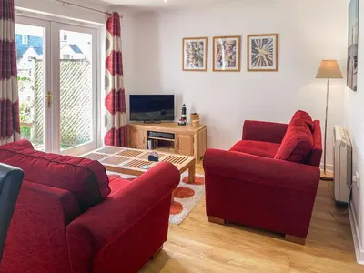 a living room with two red chairs and a television at Merizac in Budock Water