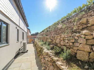 a stone wall next to a building with the sun shining at Cedar Lodge in Carbis Bay