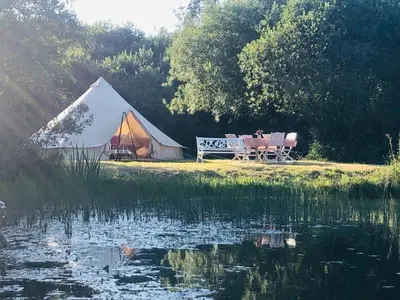 a tent with a table and a bench next to a lake at Rose in St Austell