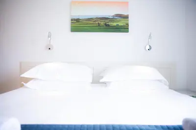 a white bed with white pillows and a painting on the wall at Trevose Golf and Country Club in Padstow