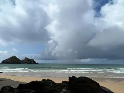 a beach with rocks and the ocean with a cloudy sky at Cornish Crantock Holiday Sandy Toes in Crantock