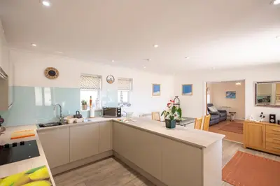a kitchen with white cabinets and a living room at Mermaid - Pet Friendly Self Catering Holiday Cottage Hayle in Hayle