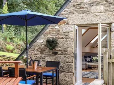 a patio with a table with a blue umbrella at Potters Barn in Helston