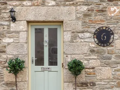 a stone house with a white door and a clock at Potters Barn in Helston