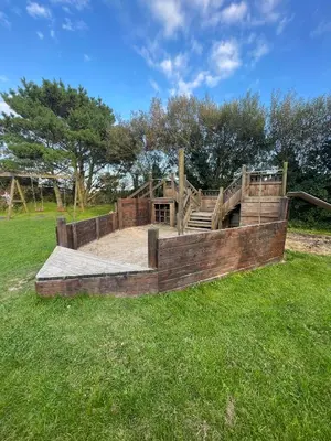 a wooden playground in a field with grass at Stones Throw Lodge in Padstow