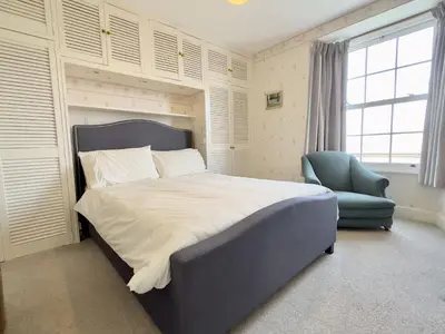 a bedroom with a large bed and a blue chair at Coswarth Cottage in Padstow