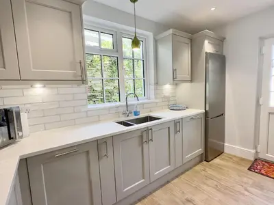 a kitchen with white cabinets and a sink and a refrigerator at Coswarth Cottage in Padstow