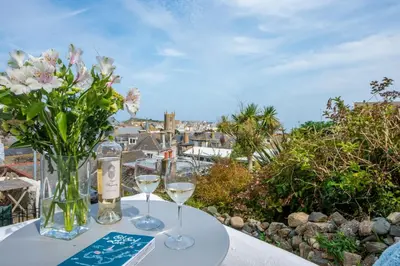 a table with two wine glasses and a vase of flowers at Cottage By The Sea, Wi-Fi, Pets Accepted in St Ives