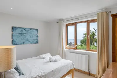 a white bedroom with a bed and a window at Rosemerryn in Marazion