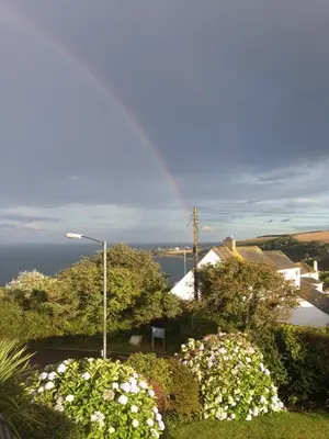a rainbow in the sky over a house with flowers at Mevagissey Boutique Flatlet with sea and countryside views in Mevagissey