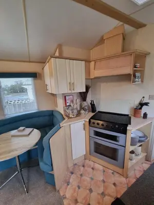 a small kitchen with a stove and a blue couch at Seven Bays Holiday Home in Padstow