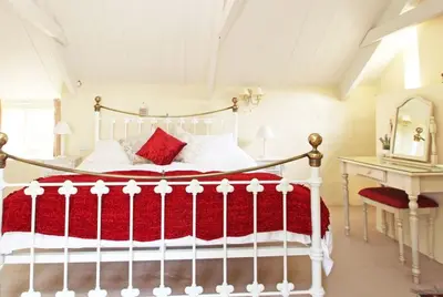 a bedroom with a white bed with a red blanket at Meadowside Cottage, Characterful Grade 2 Listed Cottage near to Wadebridge and Padstow in Wadebridge