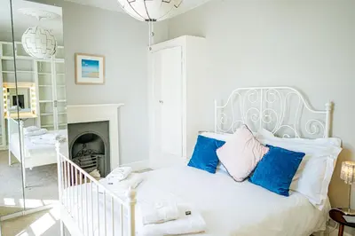 a white bedroom with a white bed with blue pillows at Marazion Beach Town House with Private Parking in Marazion