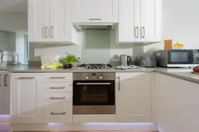 a kitchen with white cabinets and a stove top oven at Shearwater View, 7 Rosemorran, St Ives in St Ives