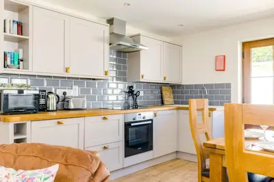 a kitchen with white cabinets and a table at Chy Pol in Wadebridge