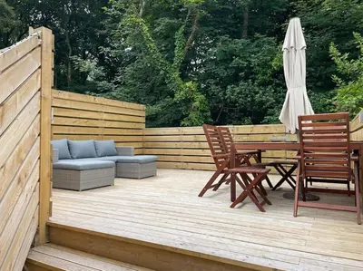 a wooden deck with a table and chairs and an umbrella at The Anvil, 2 bed cottage, in the heart of Cornwall in Gwennap