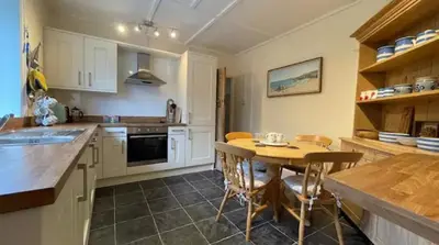 a kitchen with white cabinets and a wooden table at Seagulls Porthcothan Bay Cottage in Padstow