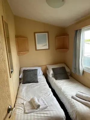 two beds in a small room with a window at Newquay Bay Porth Caravan - 8 Berth in Newquay