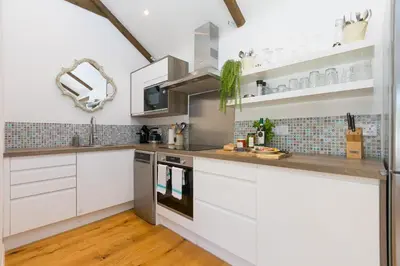 a kitchen with white cabinets and stainless steel appliances at Carines Barns - Tre in Newquay