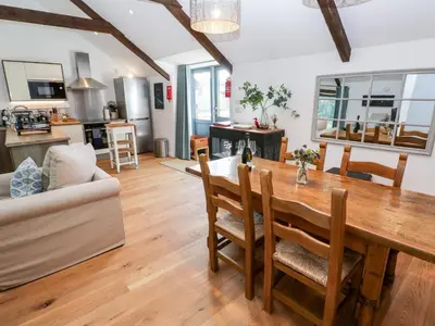 a kitchen and living room with a wooden table and chairs at Carines Barns - Pol in Newquay