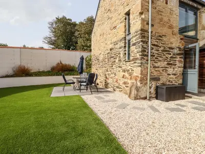 a patio with chairs and a table in a yard at Carines Barns - Pol in Newquay