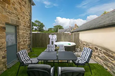 a patio with a table and chairs and a tub at Carines Barns - Pen in Newquay