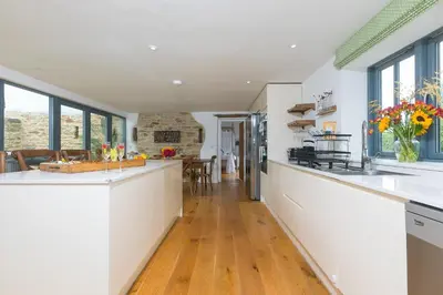 a large kitchen with white countertops and windows at Carines Barns - Wesley Barn in Newquay