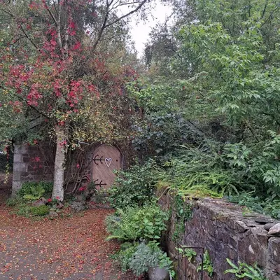 a garden with a stone fence and flowers and a gate at The Dovecote in Launceston