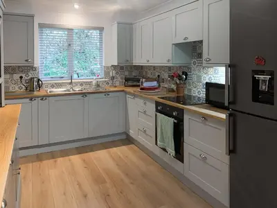 a kitchen with white cabinets and wooden floors at Stream Side in Budock Water