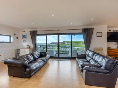 a living room with leather couches and a large window at Tregarden in Bude