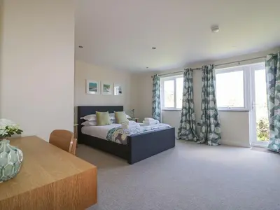 a bedroom with a bed and a table and windows at Lower Mellan Barn in Helston