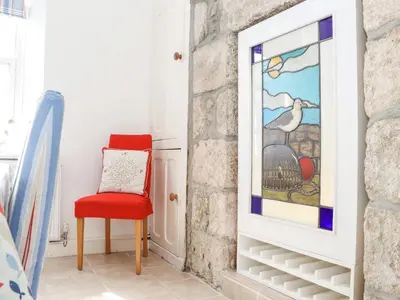 a red chair in a room with a painting on the wall at Crab Pot Cottage in Helston